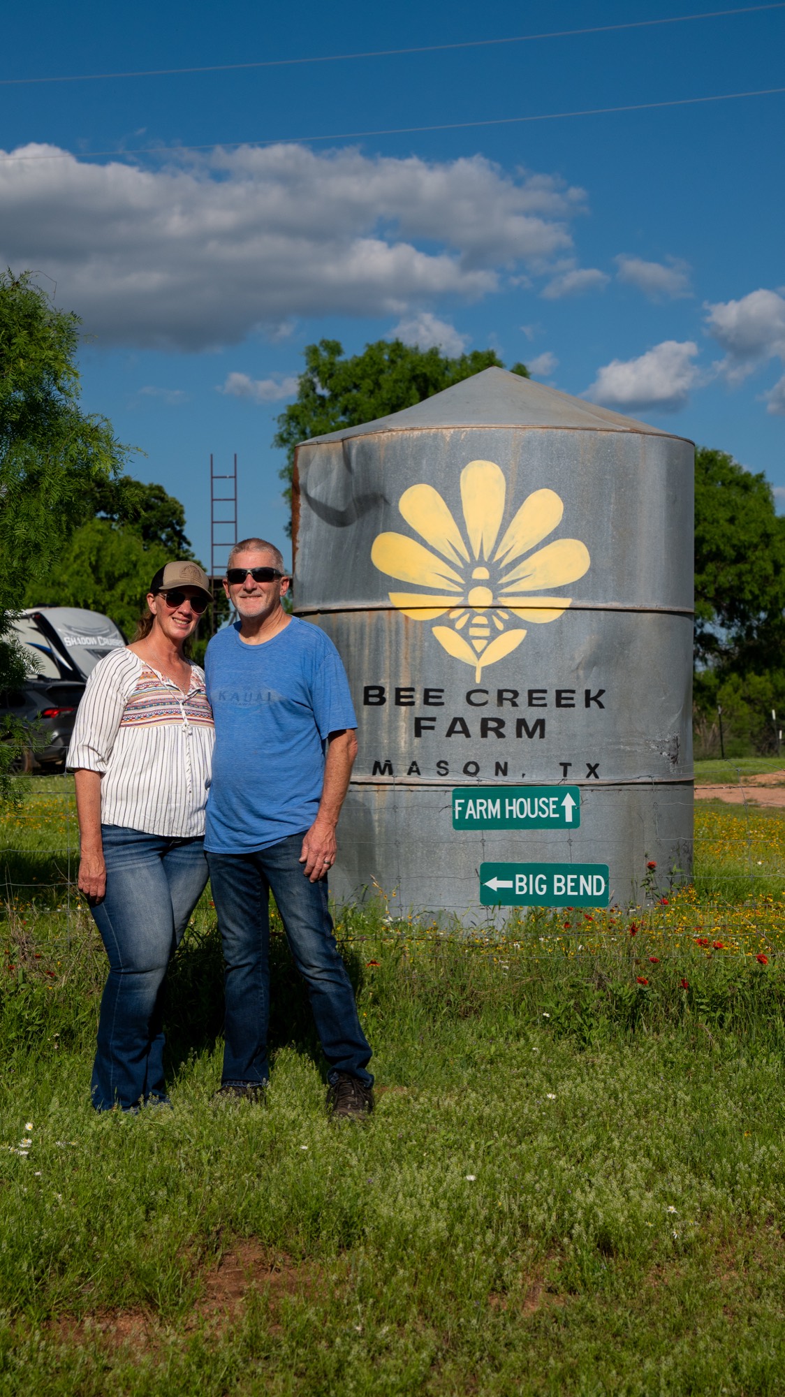 The owners of Bee Creek Farm standing in front of the painted silo with the bee-and-flower mark